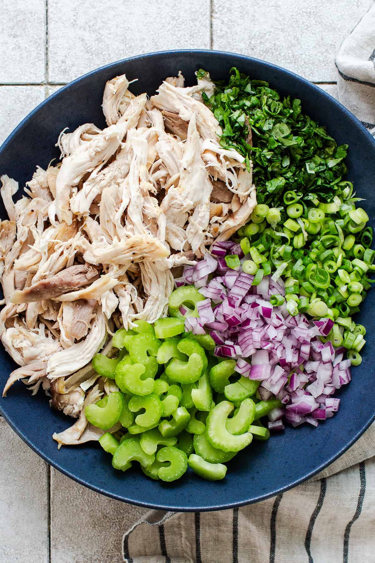 Shredded chicken, celery, red onion, cilantro, and green onion in a large bowl for chipotle chicken salad.