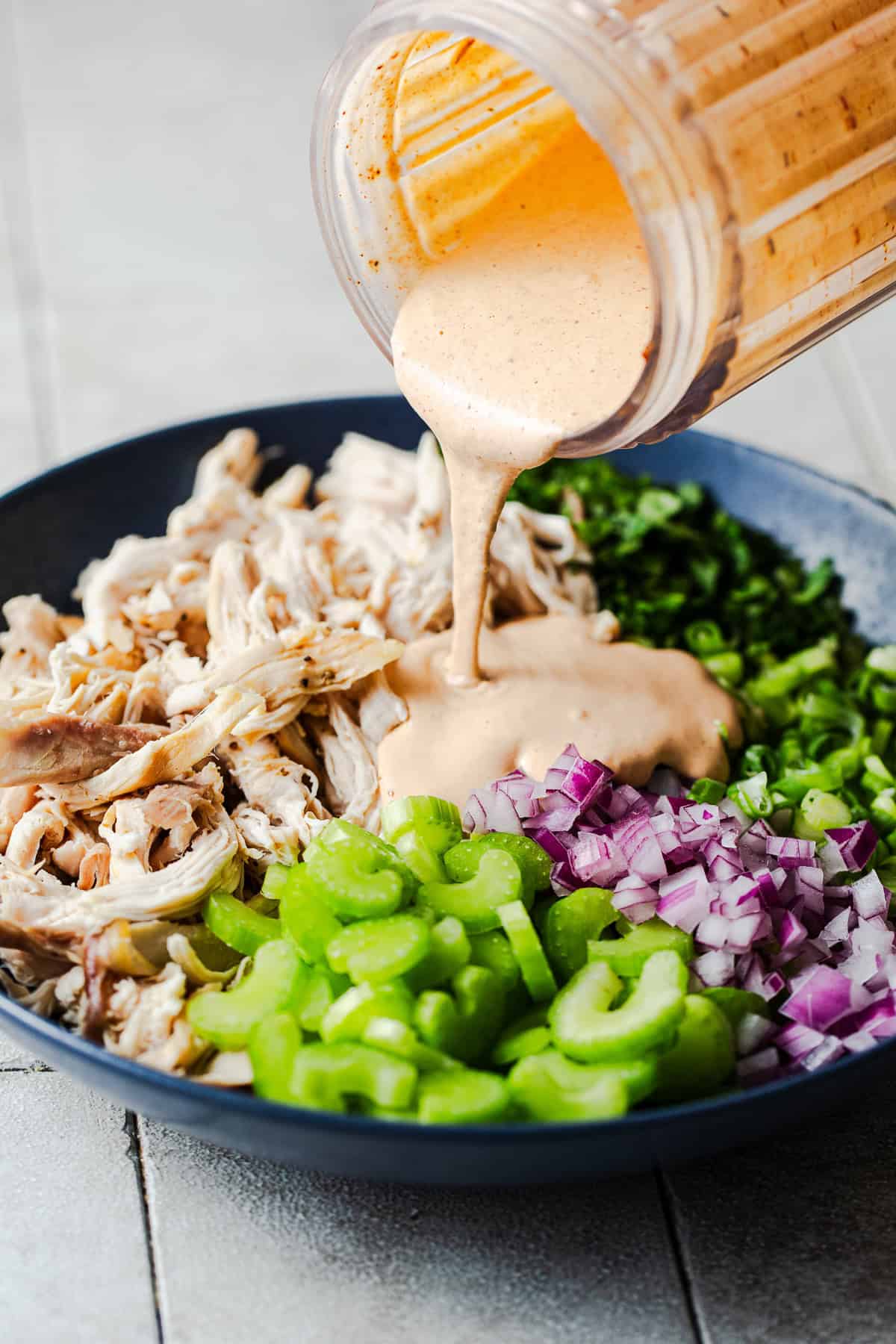 Chipotle dressing being poured over shredded chicken and veggies.