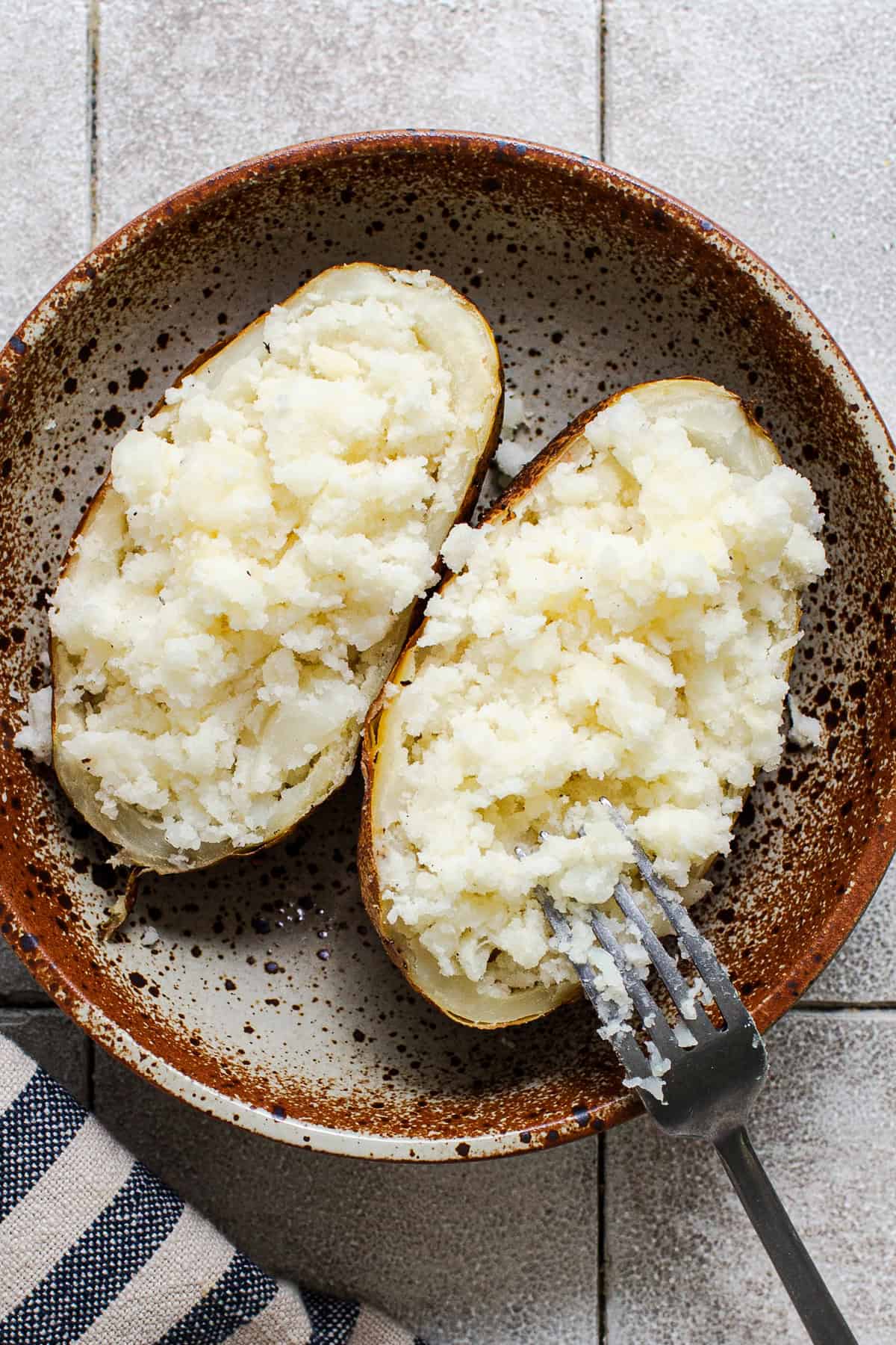 A fork fluffing the inside of a baked russet potato for papas locas.