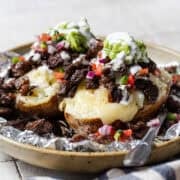Papas locas loaded with carne asada, melted cheese, pico de gallo, guacamole, and crema in foil.