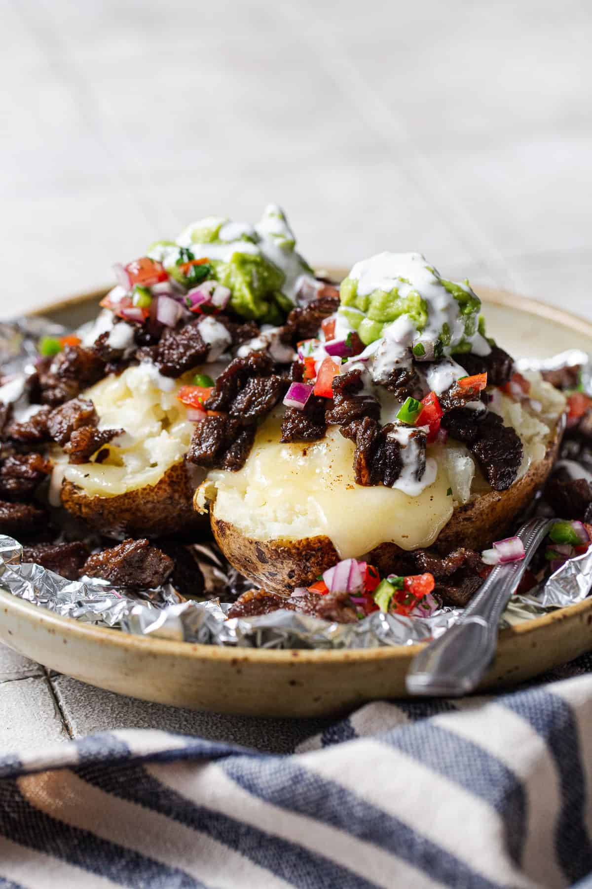 Papas locas loaded with carne asada, melted cheese, pico de gallo, guacamole, and crema in foil.