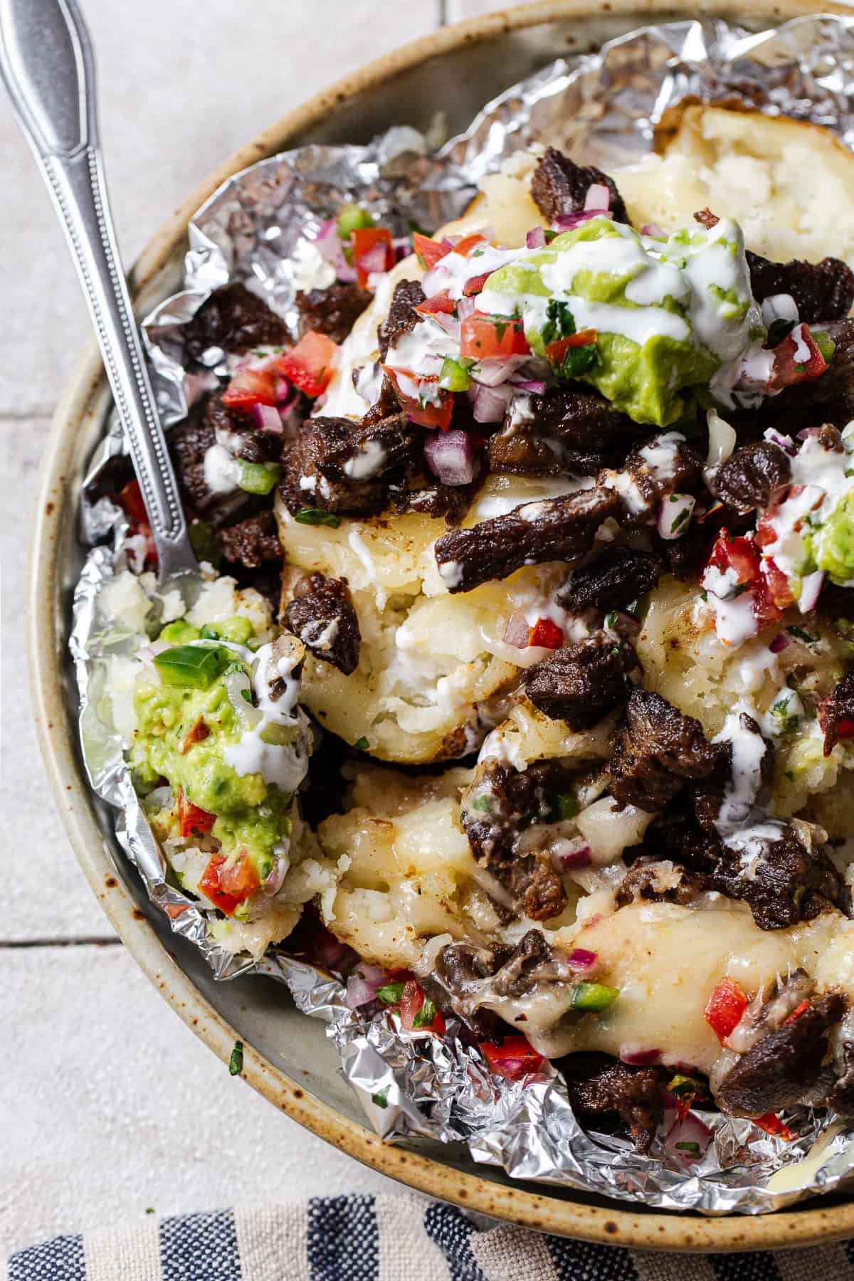 A forkful of carne asada papas locas on a plate with guac, crema, and pico.