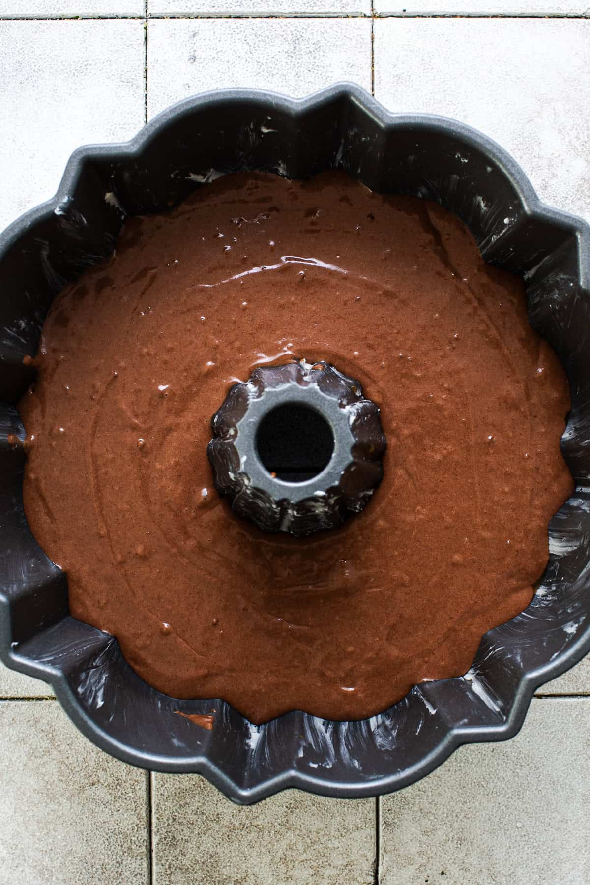 Chocolate cake batter spread in a bundt pan over cajeta for pumpkin chocoflan.