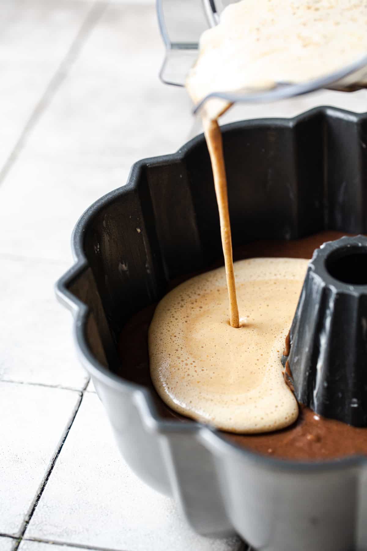Pumpkin flan mixture being poured over chocolate cake batter in a bundt pan.