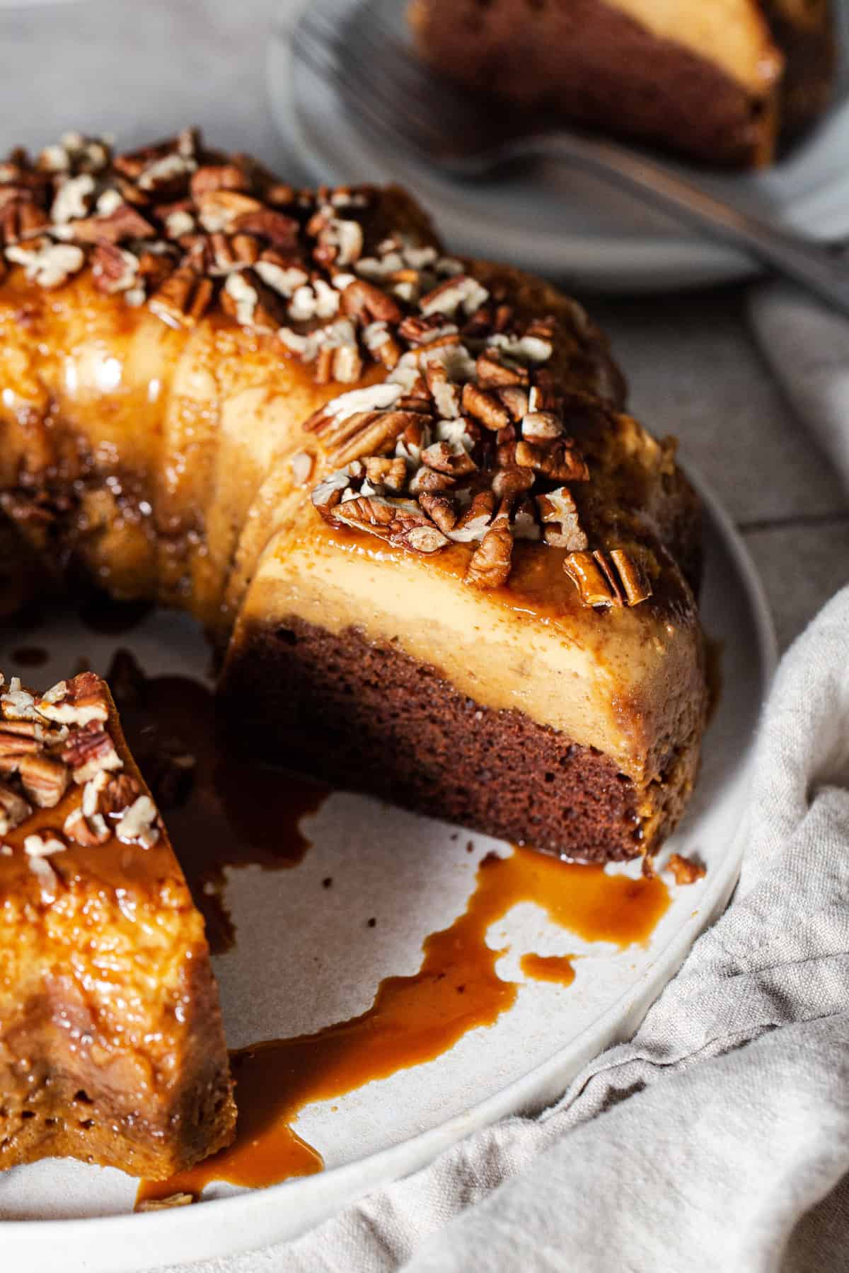 Pumpkin chocoflan topped with cajeta and chopped pecans on a serving plate with a slice cut out.