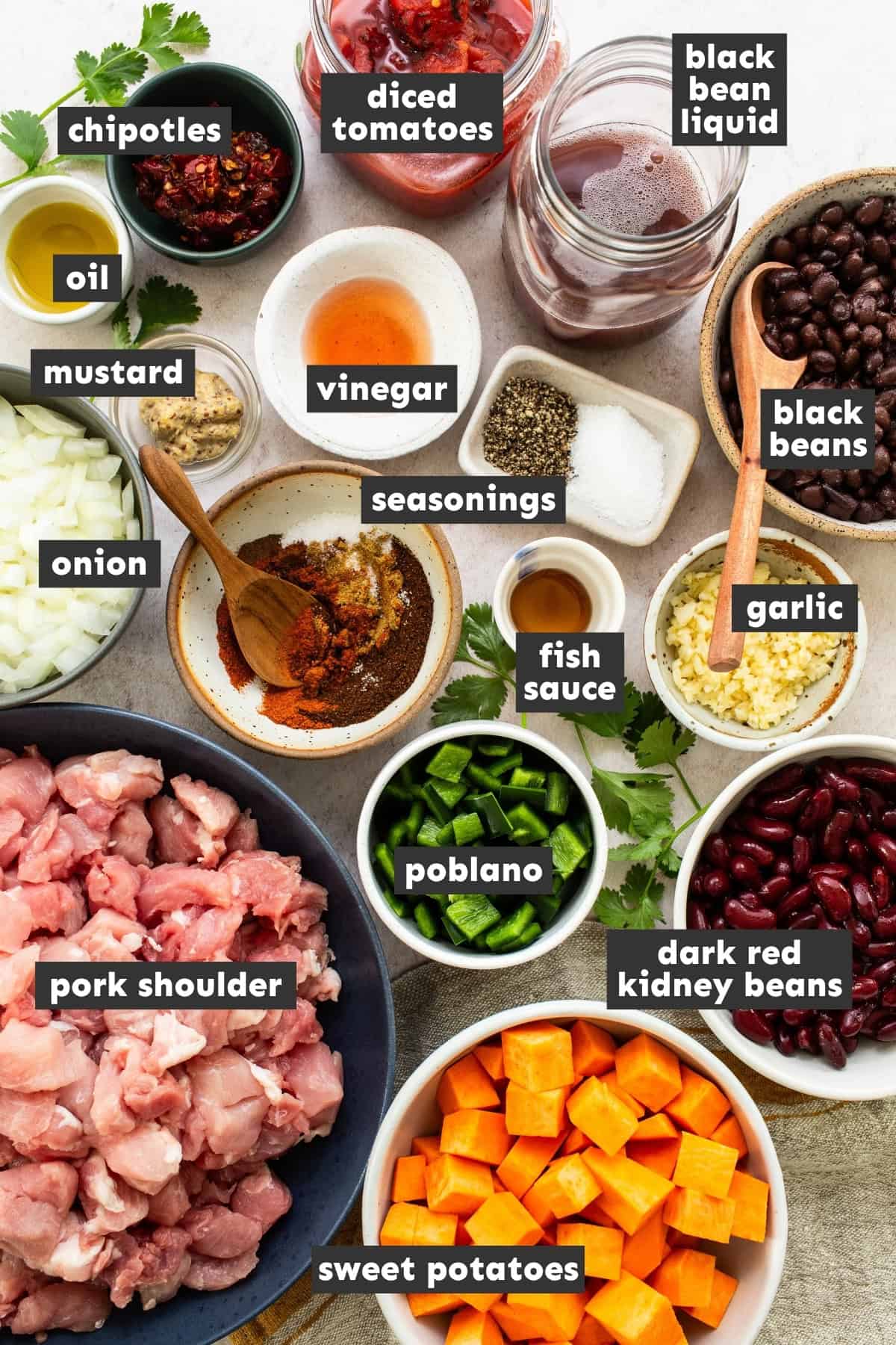 Ingredients for sweet potato chili, including pork shoulder, sweet potatoes, a poblano, canned beans, chipotles in adobo, and spices.