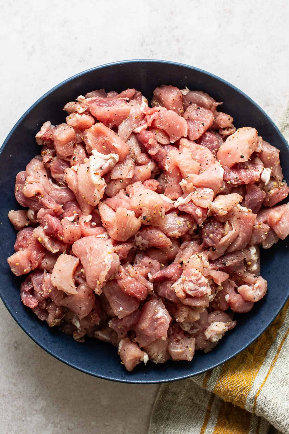 Cubed pork shoulder coated in salt, pepper, and coarse-ground mustard in a large bowl.