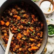 Finished sweet potato chili with pork in a Dutch oven with toppings on the side.