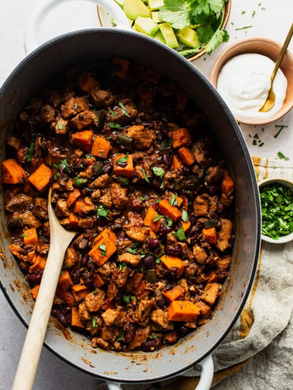 Finished sweet potato chili with pork in a Dutch oven with toppings on the side.