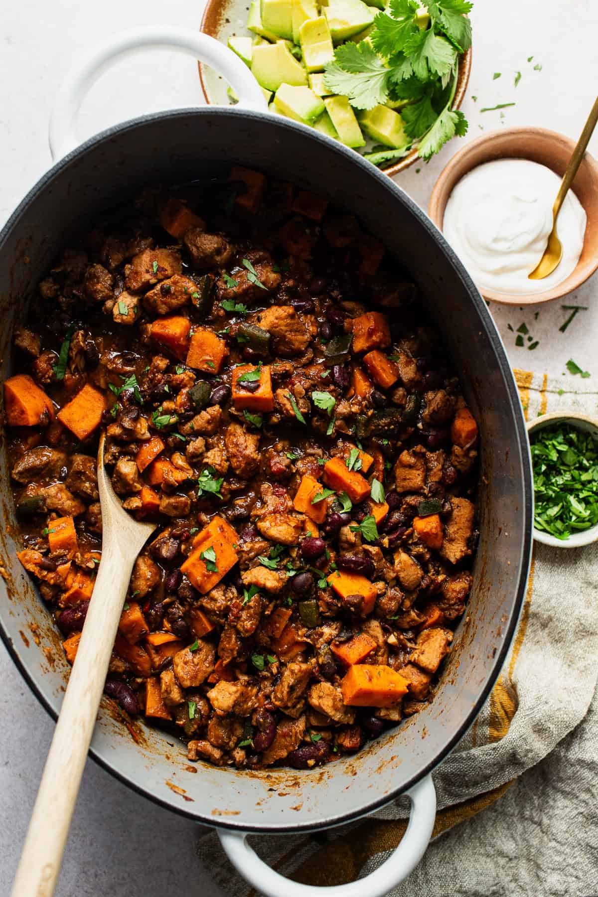 Finished sweet potato chili with pork in a Dutch oven with toppings on the side.