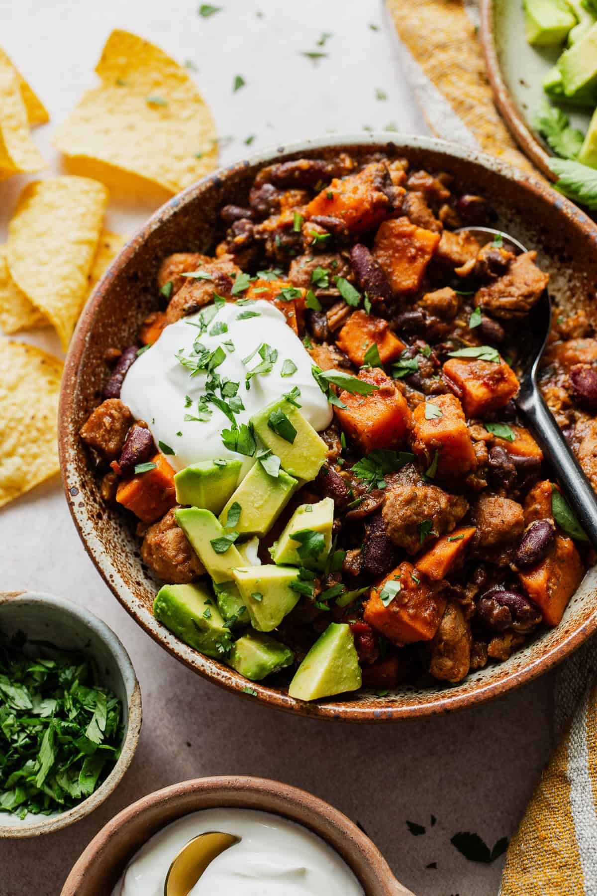 A bowl of sweet potato chili topped with sour cream, cilantro, and avocado, with tortilla chips.