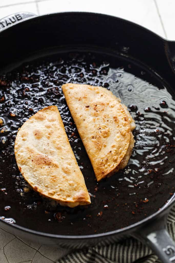 Tacos de papa shallow frying in a skillet.
