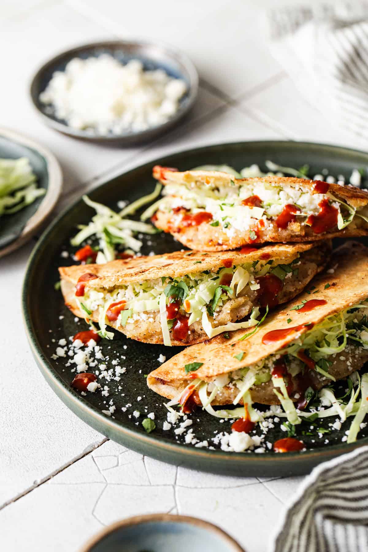 A plate with crispy potato tacos, aka tacos de papa, stuffed with thinly shredded cabbage, cotija cheese, and hot sauce.