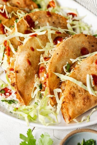 Crispy tacos de papa stuffed with shredded cabbage and cotija cheese, drizzled with hot sauce.