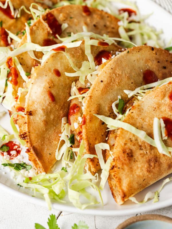Crispy tacos de papa stuffed with shredded cabbage and cotija cheese, drizzled with hot sauce.