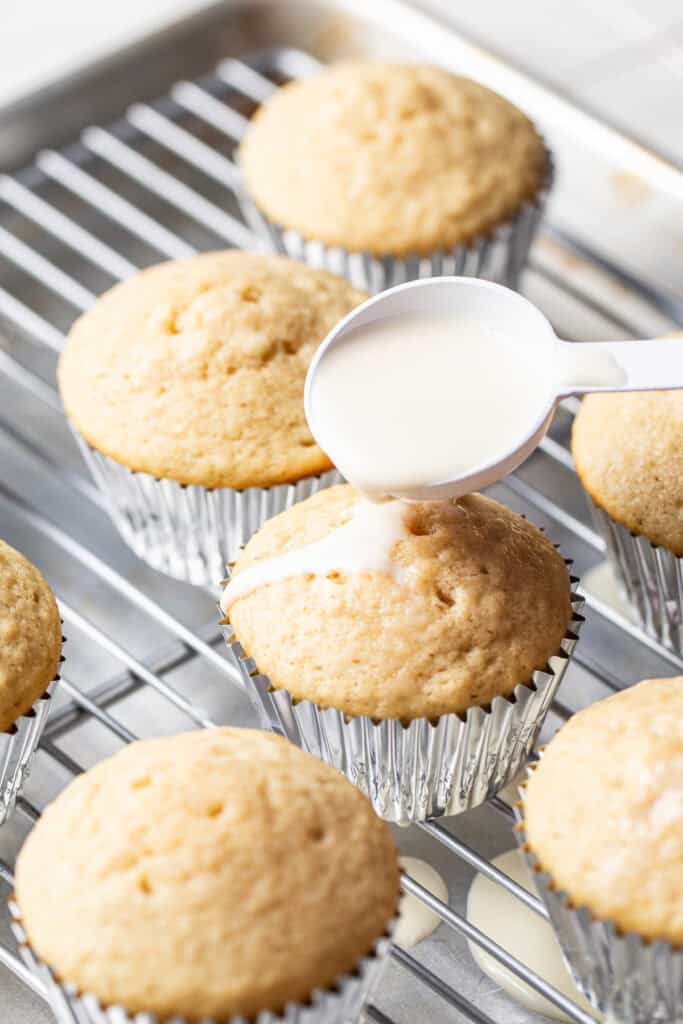 Spooning the three-milk mixture over a tres leches cupcake with holes poked in the top.