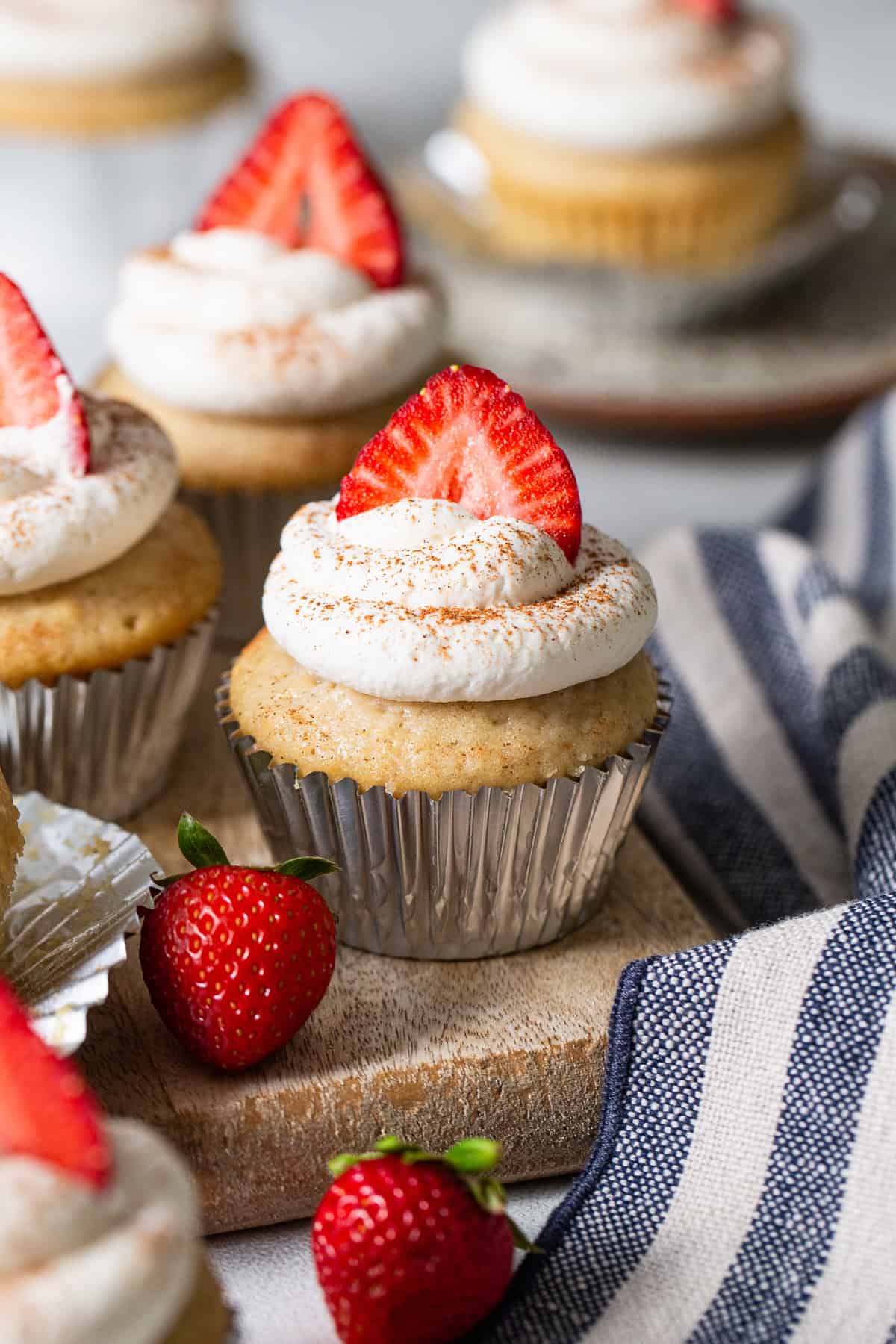Tres leches cupcake topped with piped whipped cream, cinnamon, and sliced strawberries.