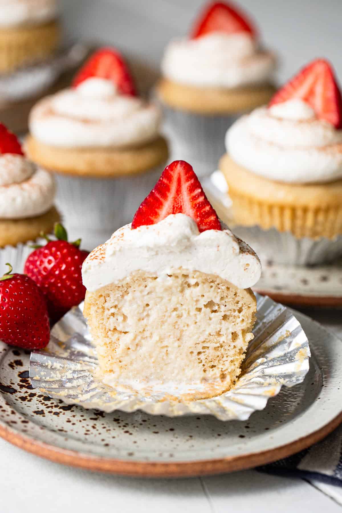 Tres leches cupcake with the liner peeled back and a bite taken out, showing the soaked inside.