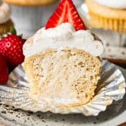 Tres leches cupcake with the liner peeled back and a bite taken out, showing the soaked inside.