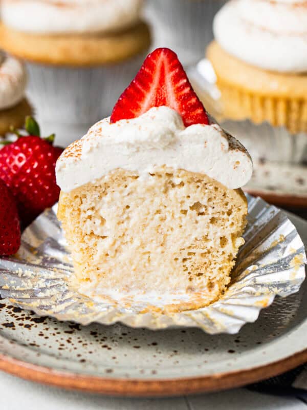 Tres leches cupcake with the liner peeled back and a bite taken out, showing the soaked inside.