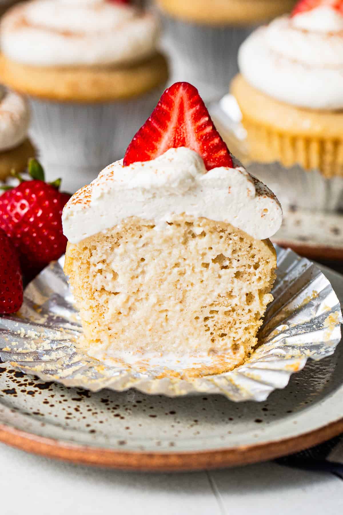 Tres leches cupcake with the liner peeled back and a bite taken out, showing the soaked inside.